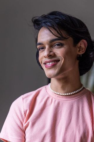 Smiling asian man wearing pink textured top and pearl necklace, elegant studio portrait