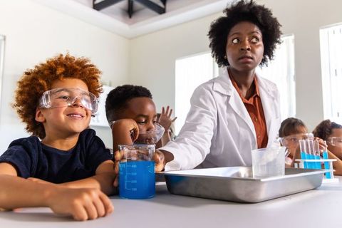African american teacher guiding students conducting chemistry experiment with beakers