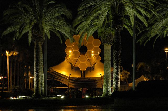 Full-scale James Webb Space Telescope model illuminated among palm trees at night. NASA and Northrop Grumman built this model to demonstrate the telescope's size and structure. Useful for content on space technology exhibits, astronomical advancements, and public science outreach.