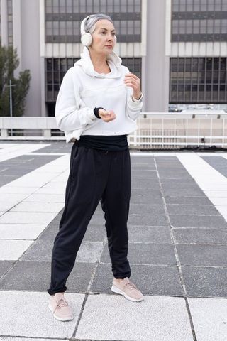 Senior woman pausing on rooftop checking smartwatch after urban walk in hoodie and headphones