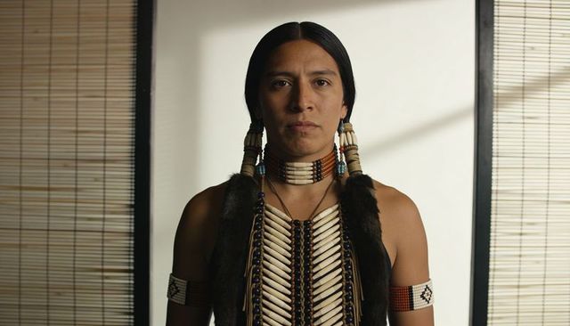 Standing native american man wearing bone breastplate and beadwork, traditional portrait
