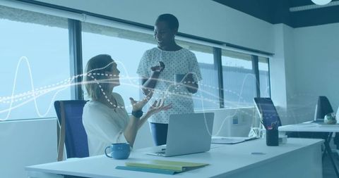 Two women collaborating on data analytics at laptop in modern open-plan office