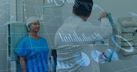 Radiology technician adjusting digital x-ray gantry with senior woman in blue gown waiting