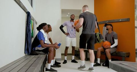 Coach delivering motivational talk to diverse male basketball team in locker room pre-game