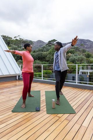 African american couple practicing yoga on rooftop terrace with mountain views