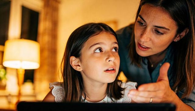 Mother guiding daughter using tablet at home during evening learning and screen time