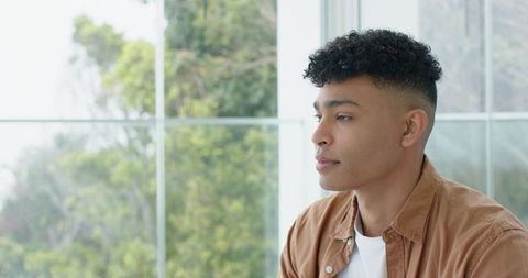 Contemplating young man sitting by window in bright modern room with natural light