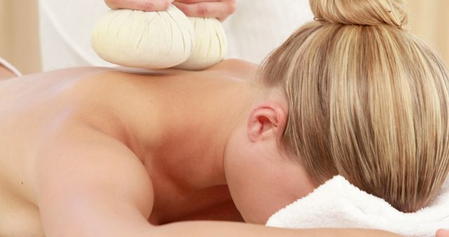 A Caucasian woman enjoys a relaxing spa treatment with herbal compresses on her back, with copy space. Spa therapies like this are designed to promote relaxation and well-being.