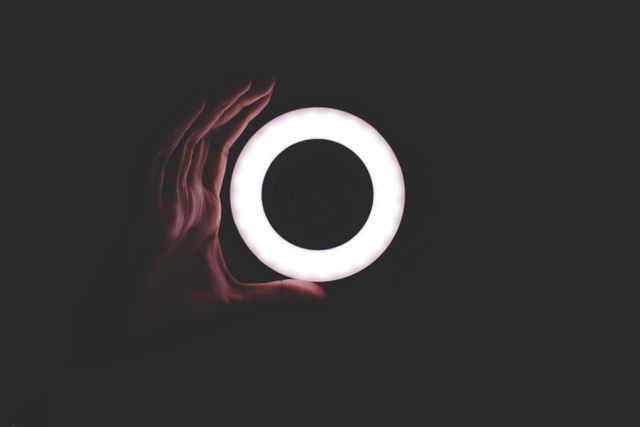 Hand holding a circular, glowing light source in a dark environment. Suitable for technology, design, and creative projects. Perfect for backgrounds, conceptual images, and minimalist designs.