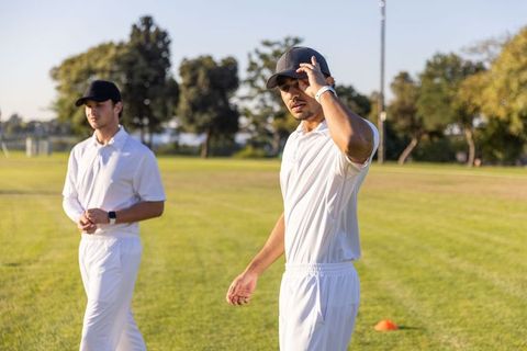 Diverse cricket players adjusting caps on sunlit field during practice at golden hour