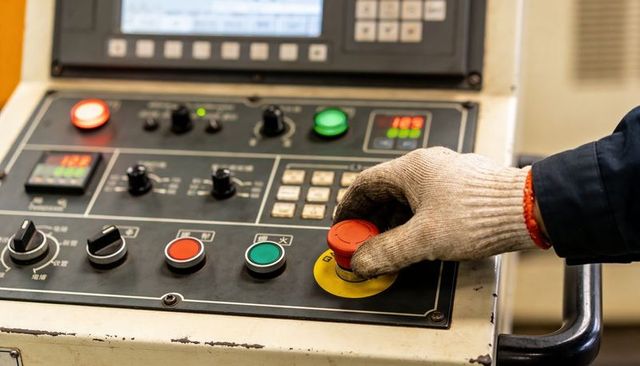 Pressing gloved hand activating emergency stop on industrial control panel, closeup