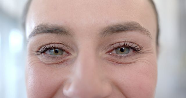 Close-up view of a smiling woman's eyes highlighting natural beauty and eyelashes. Ideal for marketing materials relating to beauty products, skincare, or happiness. Suitable for use in health and wellness blogs, cosmetic advertisements, or personal care brochures.