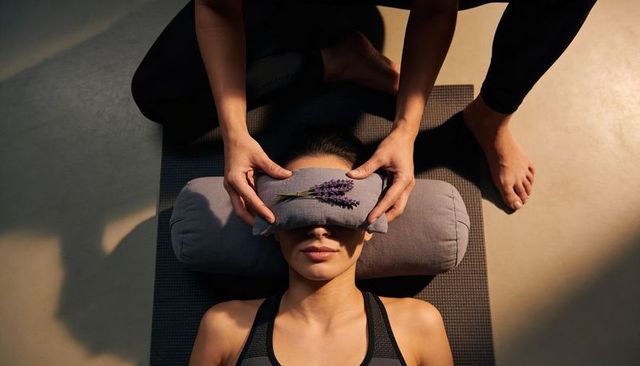 Therapist placing lavender eye pillow over client during restorative yoga relaxation