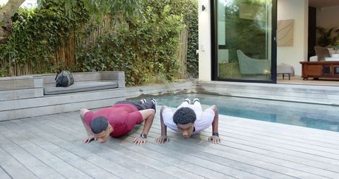 Friends exercising push-ups on wooden deck by pool