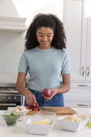 Smiling woman chopping fresh onions in modern kitchen
