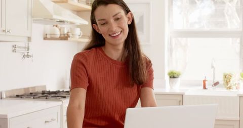 Smiling woman working on laptop in modern kitchen