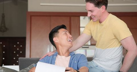Diverse Male Couple Smiling with Document at Home