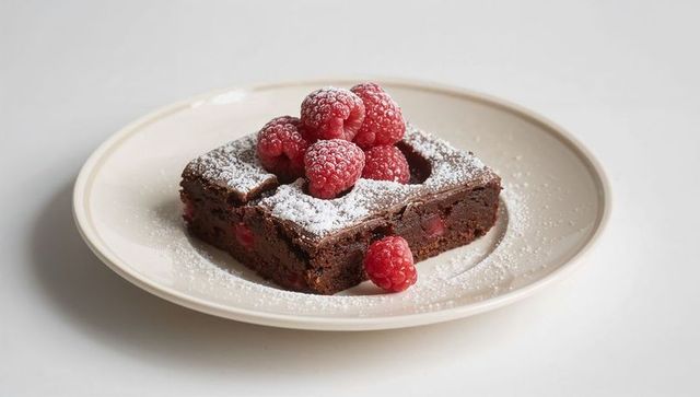 Fudgy chocolate brownie with raspberry hollow and powdered sugar on cream plate
