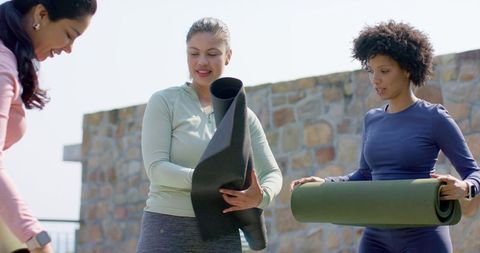 Diverse women holding yoga mats on rooftop terrace preparing for outdoor fitness class