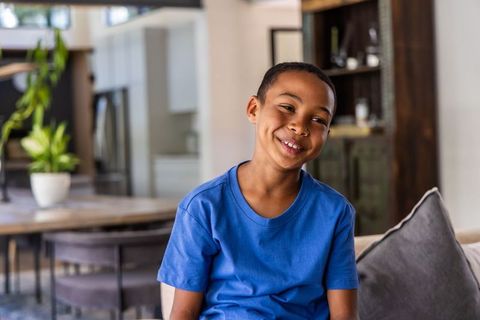Smiling african american boy sitting on couch wearing blue t-shirt in cozy open living room