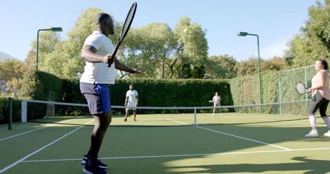 Friends Playing Doubles Tennis On Sunny Outdoor Court