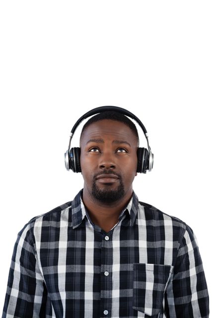 This image depicts an African American man wearing headphones and a plaid shirt, looking thoughtful against a white background. It can be used for promoting music streaming services, technology products, lifestyle blogs, or articles about relaxation and leisure activities.