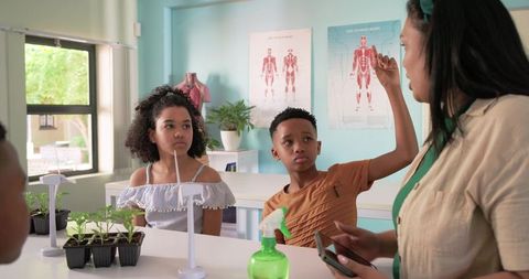 African american teen raising hand during hands-on classroom science with seedlings