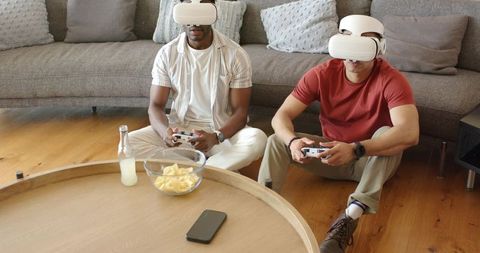 Diverse men playing VR games with white headsets and controllers in modern living room