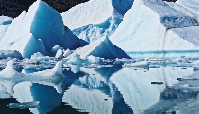 Cerulean iceberg reflections in glacier lagoon with multi-peaked icebergs and floes