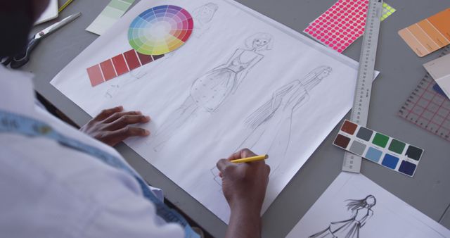 Designer sketches fashion illustrations in a studio. Creative process unfolds with color palettes and fabric samples on the table.
