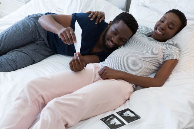 Man and pregnant woman looking at sonography in bedroom at home