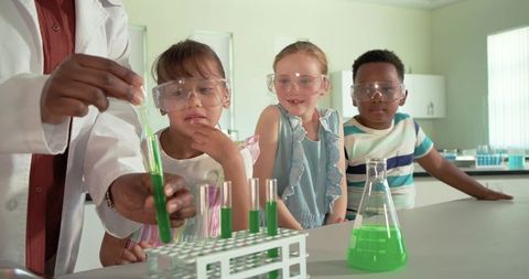 Diverse students observing chemistry demonstration with instructor and green solution