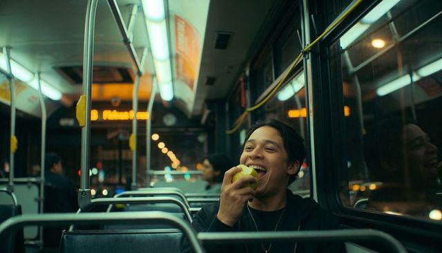 Smiling young man biting green apple on night bus during relaxed urban commute