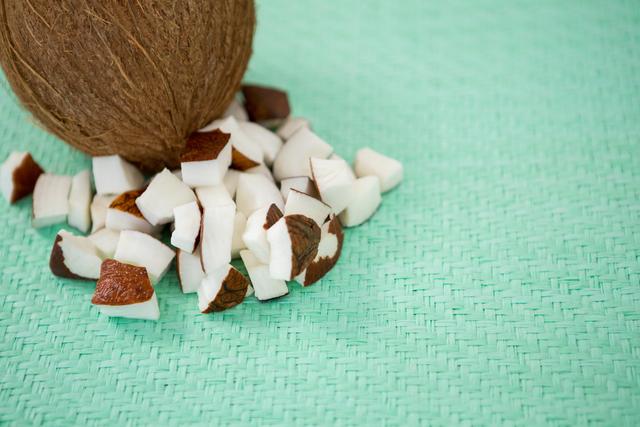 Close-up of whole coconut and diced coconut pieces on a green woven surface. Perfect for blogs, articles, and advertisements about healthy eating, tropical fruits, vegan recipes, and natural ingredients.