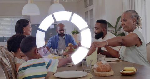 Multigenerational family sharing meal at kitchen table, passing dishes and bread