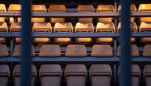 Sunlit empty stadium seats forming repeating geometric pattern on metal bleachers under warm light