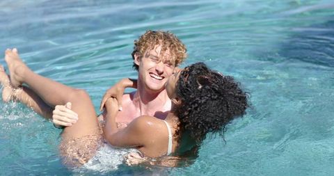 Couple embracing and kissing in turquoise pool laughing and splashing in sunlight