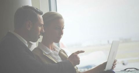 Business partners collaborating over laptop at airport gate with runway and airplane view