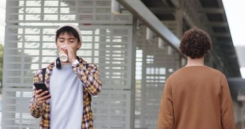 Young multicultural commuters standing on train platform drinking coffee and checking phone