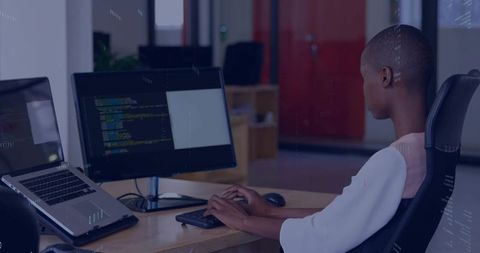 Focused developer coding on dual monitors at ergonomic workstation in modern office hub