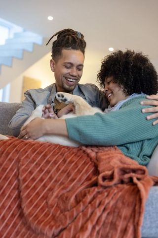 Cozy african american couple cuddling with dog on sofa wrapped in textured blanket