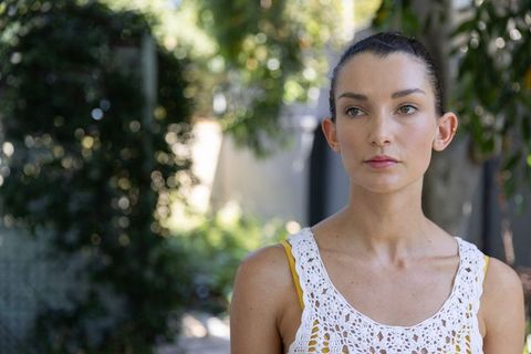 Serene woman in sunlit garden wearing white crocheted top with yellow strap