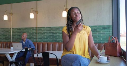 Woman recording voice message at cafe counter enjoying coffee and casual work vibe