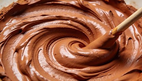 Stirring glossy chocolate batter with wooden spatula forming creamy swirls close-up