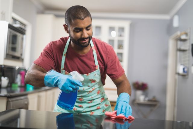 Young man cleaning marble counter in kitchen at home