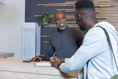 African american receptionist smiling while assisting visitor signing form at modern desk
