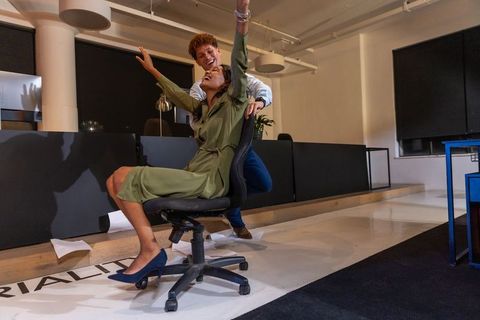 Diverse coworkers spinning office chair during late-night teamwork celebration