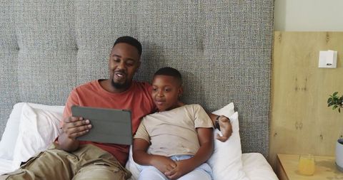 Father bonding with son over gadget in cozy bedroom setting