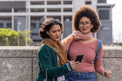 Friends leaning on urban railing checking phone with confused expressions