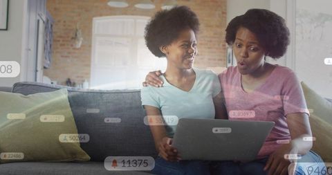 Mother daughter watching laptop on couch reacting to social notifications and learning